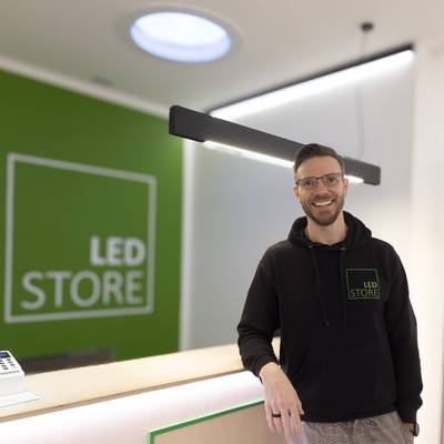 Muž v LED STORE-huvtröja vid belysningsdisk, zelený LED-skylt, moderní prostředí butiku