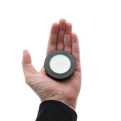 Na ruce je zobrazeno kruhové stropní svítidlo LED s bílým difuzorem a černým rámečkem na hladkém bílém pozadí.