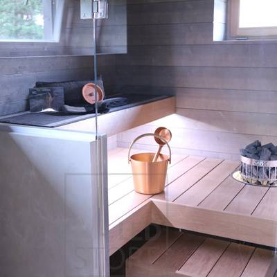 Moderní interiér sauny s dřevěnými lavicemi, skleněnými dveřmi, měděnou nádrží na vodu na podlaze a topnými kameny v rohu. Ideální pro vylepšení LED osvětlení.