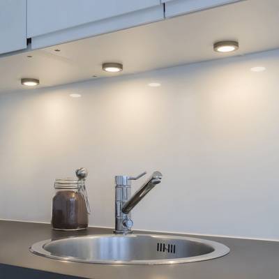 Tři LED světla pod skříňkou osvětlují zadní desku v blízkosti moderní kuchyňské baterie a skleněné nádoby.