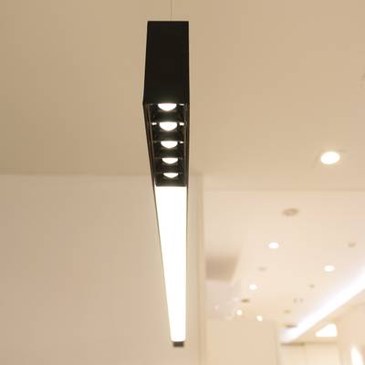 Moderní černé závěsné svítidlo s jasnou bílou září v minimalistické místnosti, které podtrhuje moderní styl a energeticky úsporné osvětlení.