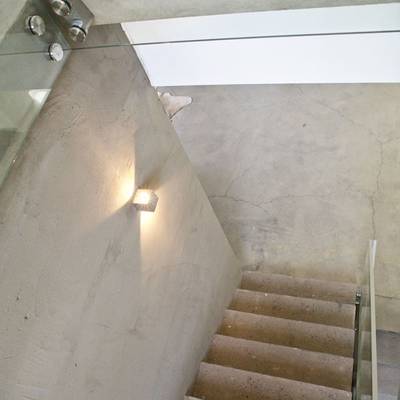 Moderní schodiště s betonovými stupni, skleněným zábradlím a nástěnným LED světlem, které hřejivě svítí; minimalistický design dotváří atmosféru.