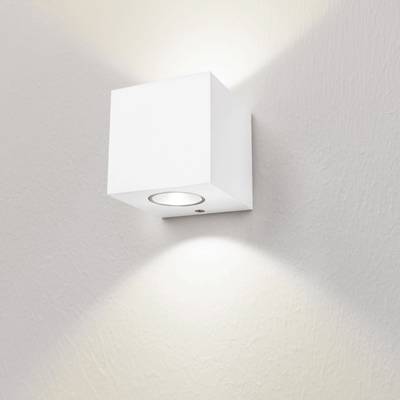 Minimalistické bílé nástěnné svítidlo ve tvaru kostky osvětluje jemně strukturovanou bílou stěnu světlem směřujícím nahoru a dolů. Ideální pro moderní LED osvětlení.