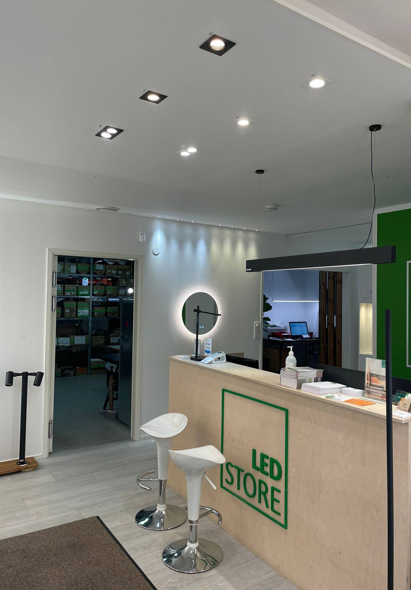Led světla v showroomu společnosti Ledstore. Bodová světla na stropě před pultem a stropní světlo VIIVA nad pultem. Stěna je zvýrazněna 3W bodovými sadami, pevnými a směrovými. Zrcadlo Moon 600 light pod spoty. Ledstore.fi