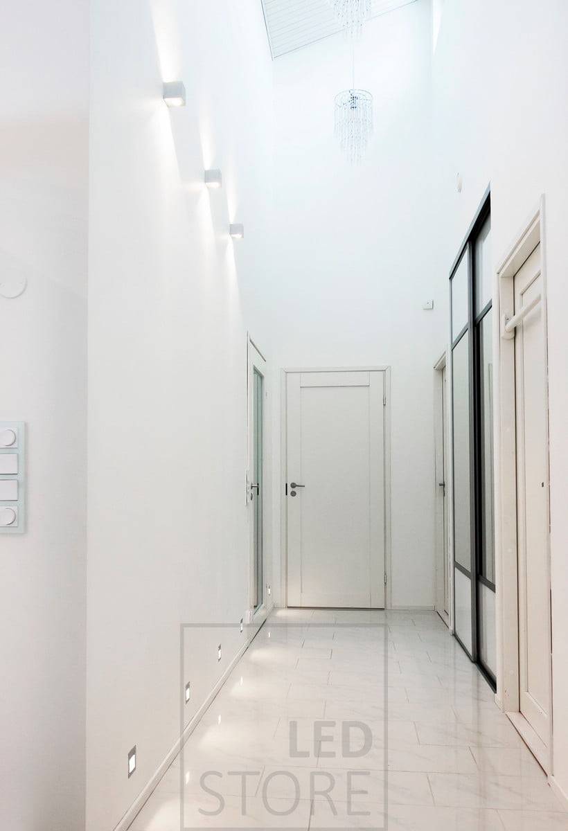 Nástěnné svítidlo CUBIC led svítící ve dvou směrech v chodbě pro zvýraznění výšky prostoru. Zapuštěná led nástěnná svítidla na hranici podlahy poskytují nepřímé světlo na podlahu. Ledstore.fi