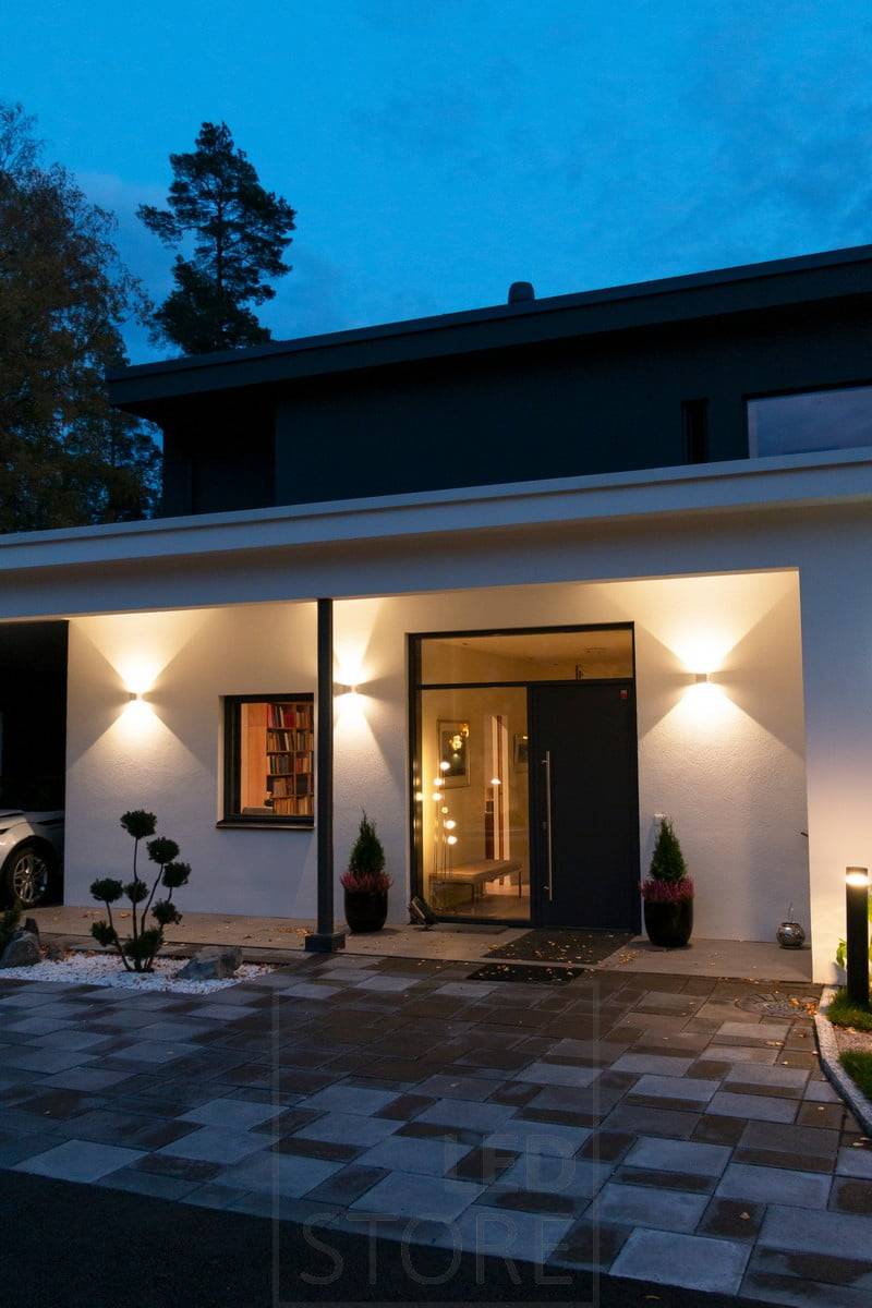 Bílá nástěnná svítidla FUNK na stěně budovy, která osvětlují fasádu a vytvářejí venku atmosférické osvětlení. Ledstore.fi