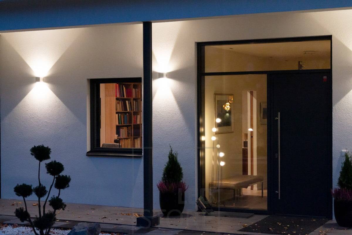 Bílá nástěnná svítidla FUNK na stěně budovy, která osvětlují fasádu a vytvářejí venku atmosférické osvětlení. Úhel světla je nastavitelný. Ledstore.fi