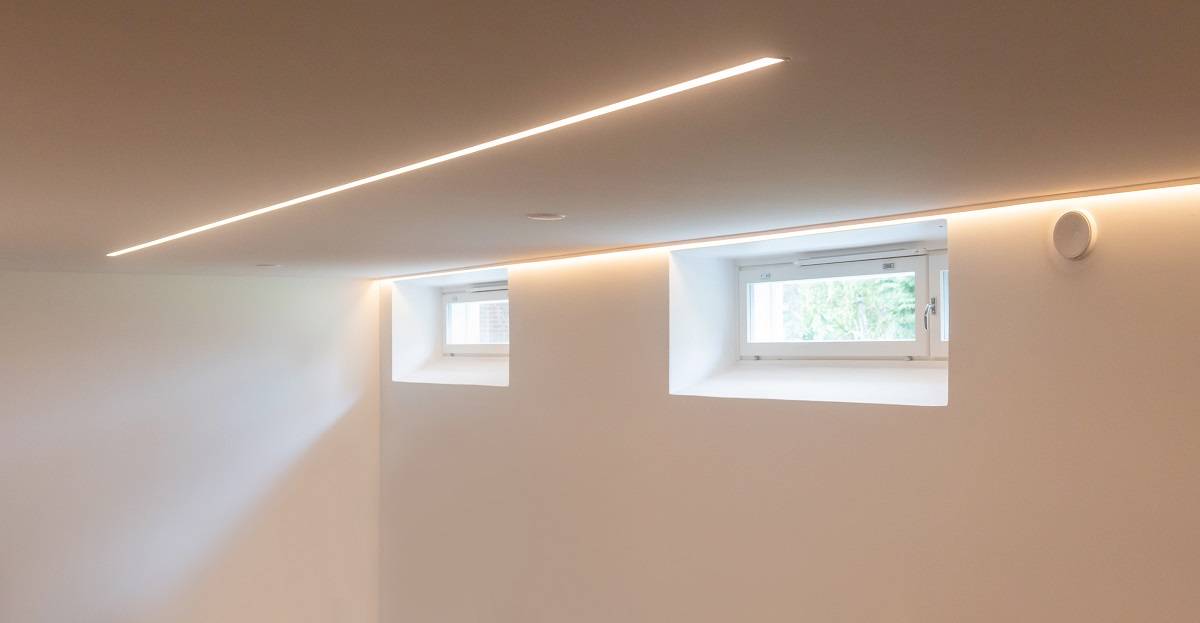 LED světelný pás podél stěny za lištou a zapuštěný uprostřed stropu.