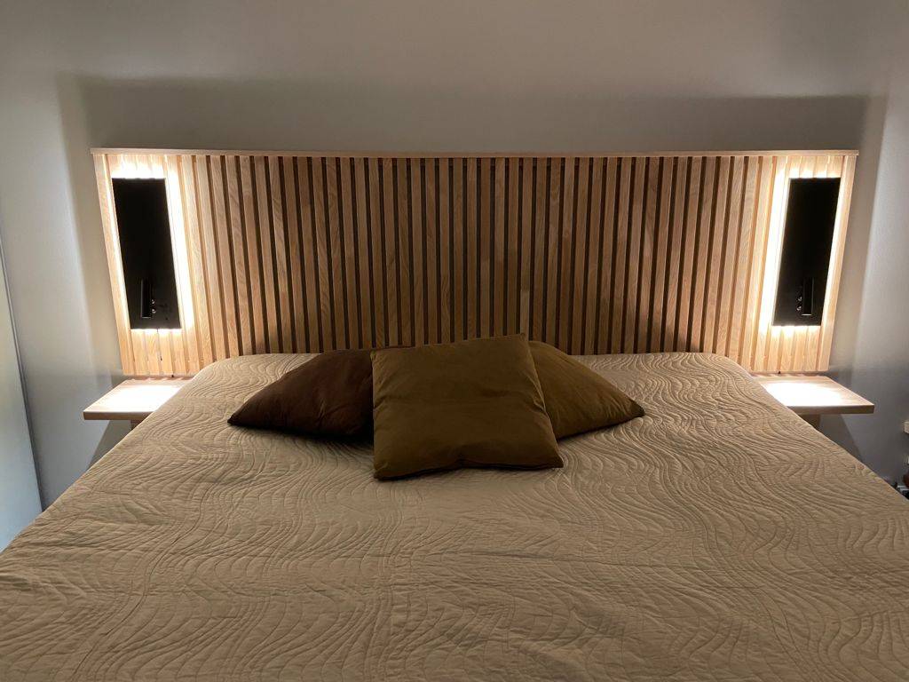 Černé nástěnné lampy NIGHT u čela postele. Svítidlo má směrové světlo na čtení a nepřímé náladové světlo. Ledstore.fi