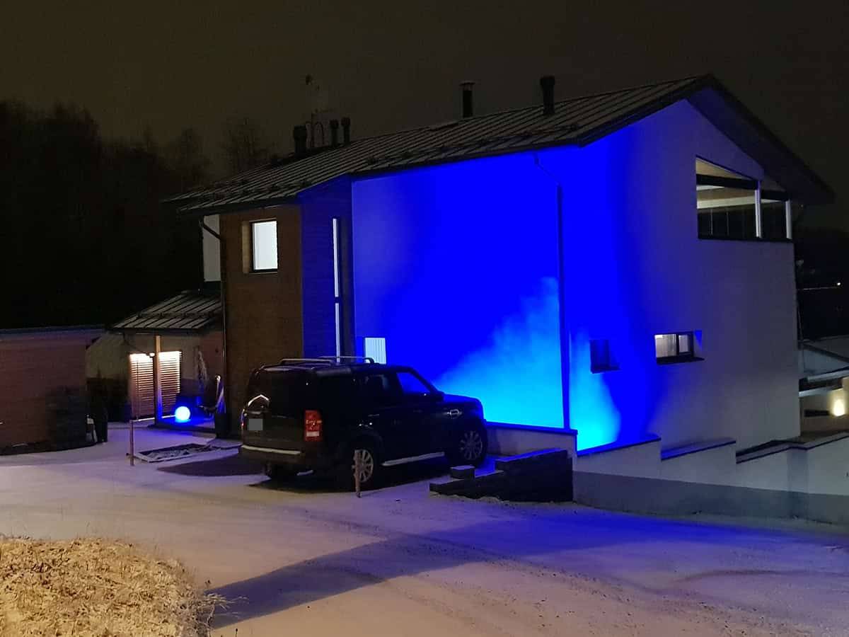 Fasáda moderního domu osvětlená v noci modrými světly LED. Auto na dvoře a lehká sněhová pokrývka na zemi.