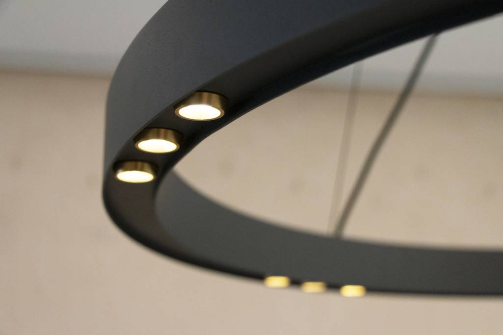 Detailní záběr moderního matně černého kulatého lustru se zapuštěnými světly LED, která vytvářejí měkkou záři na rozmazaném pozadí a vytvářejí elegantní atmosféru.