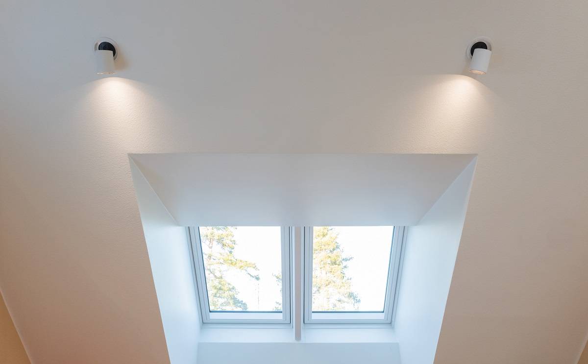 Osvětlení - Dům v jižním Espoo Bílý strop je vybaven dvěma zdvojenými svítidly LED, která jasně osvětlují střešní lucernu. Do střešního světlíku se otevírají dvě obdélníková okna, která nabízejí výhled na modrou oblohu a koruny stromů. Tuto úchvatnou sadu osvětlení si můžete pořídit na stránkách LedStore.fi, kde na vás čeká široká nabídka kvalitních LED svítidel, s nimiž si doma vytvoříte dokonalou atmosféru.