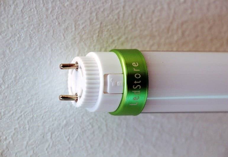 Detailní pohled na LED trubicové světlo z jednoho konce, na kterém jsou vidět dva kovové kolíky a logo LedStore.fi.