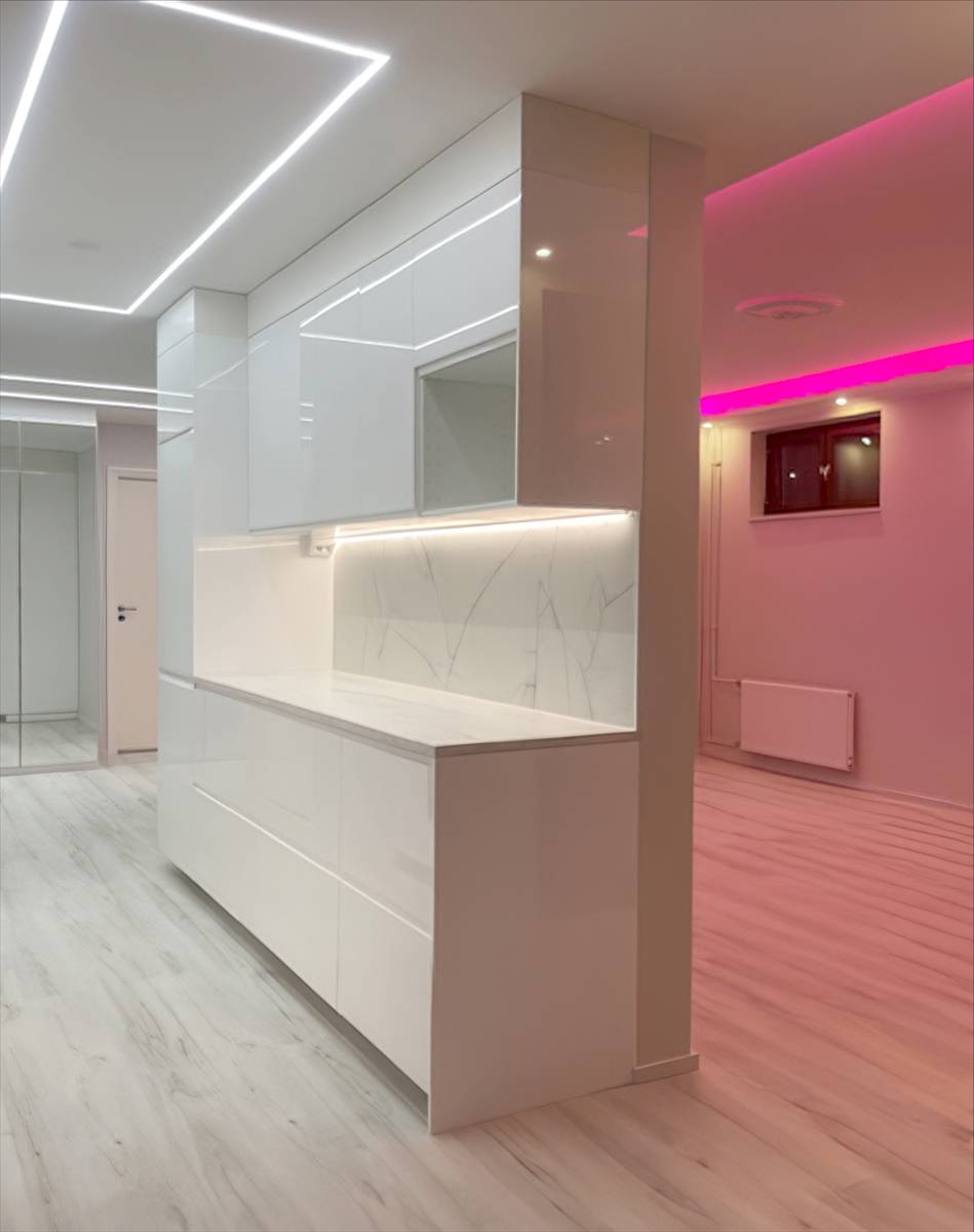 Čtvercová světelná linka na stropě kuchyně a růžové led světlo v obývacím pokoji.